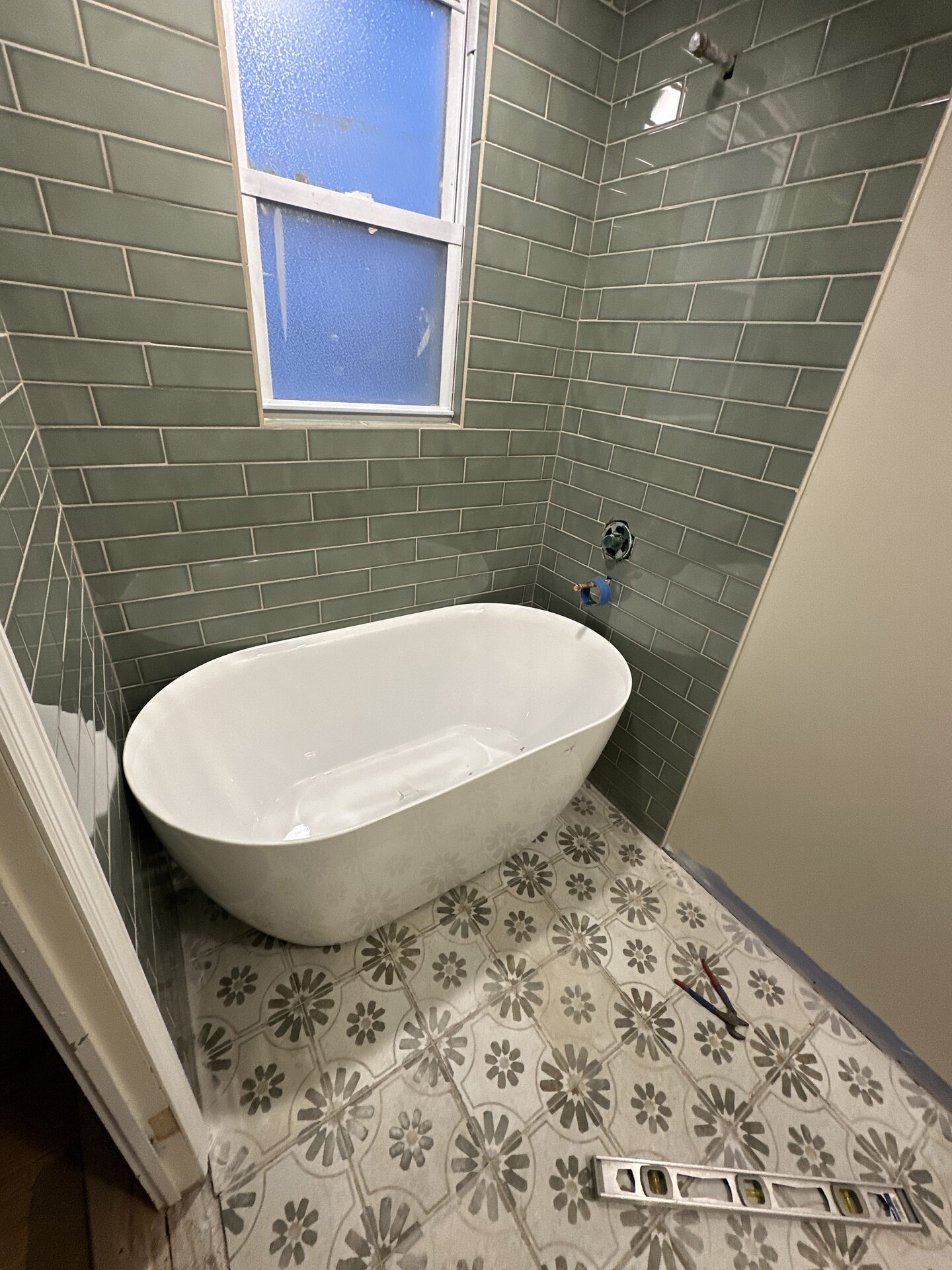 Freestanding soaking tub with sage green subway tile and patterned floor tile