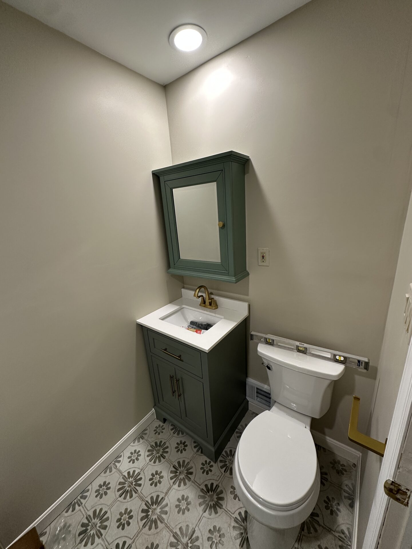 Finished powder room renovation with sage green vanity and brass fixtures