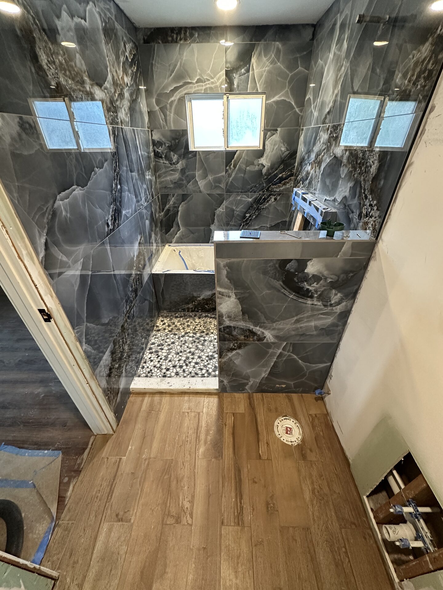 Onyx-look marble shower with black and white pebble tile floor, in-progress installation